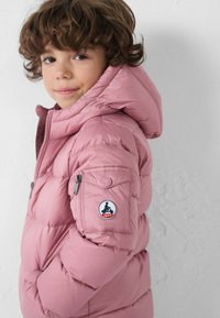 Chaqueta inflada rosa con capucha, que cuenta con un bolsillo con cremallera en la manga y un parche de logo, fabricada con un material liso y brillante.