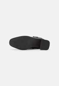 Suela de zapato de cuero negro con forma rectangular, superficie de goma texturizada y tacón cuadrado. Presenta leves surcos para un mejor agarre.
