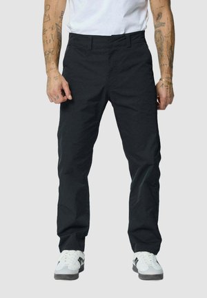 Un pantalon noir en tissu lisse, avec une coupe droite, des poches avant et une taille classique, associé à des baskets blanches.