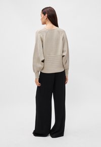 Pulover bej tricotat cu dungi texturate și talie ajustată, purtat cu pantaloni largi negri. Vizibil din spate.