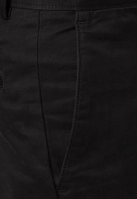 Pantaloni di cotone neri con una texture liscia, design a gamba dritta e tasche laterali. Dettagli di cucitura presenti lungo le cuciture.