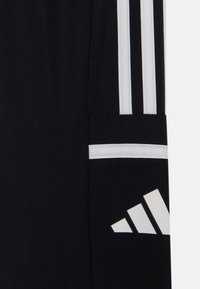 Black fabric with white Adidas logo and three white vertical stripes on sportswear material.