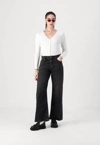 White ribbed long-sleeve top with a V-neck and button details, paired with high-waisted black wide-leg jeans and black platform shoes.