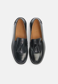 Schwarze Lederloafer mit glatter Oberfläche, runder Form, Quastenakzenten an der Vorderseite und gestickten Kanten. Die Einlegesohlen sind tanfarben.