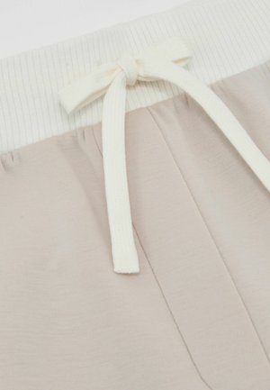 Pantaloni de trening bej deschis, cu o talie moale crem, cu dungi. Au un șnur de ajustare asortat și o textură fină pe toată suprafața materialului.