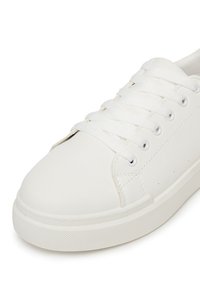 Adidași albi cu un superior sintetic neted, design cu șireturi, vârf rotunjit și talpă din cauciuc texturat. Dispune de gauri metalice pentru șireturi și detalii fine de cusătură.