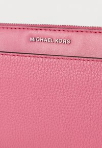 Ροζ πορτοφόλι από υφασμένο δέρμα με ασημένιο λογότυπο "MICHAEL KORS" και αντίθετη ραφή κατά μήκος του φερμουά ρ. Κοντινή εικόνα των λεπτομερειών του υλικού.