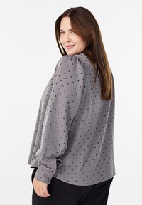 Grå skjorte med prikker, der har pufærmer, knapmanchetter og en løs pasform. Lavet af et glat stof med en blød tekstur.