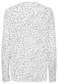 Blouse blanche à manches longues avec un motif à pois bleu marine, rose clair et marron. Tissu lisse, coupe décontractée et poignets à boutons.