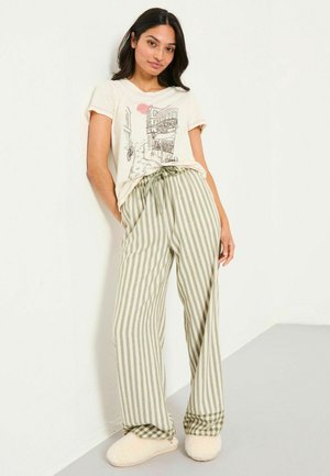 Cream t-shirt with a line drawing and a sun graphic, paired with green and white striped wide-leg pants and cream fuzzy slippers.