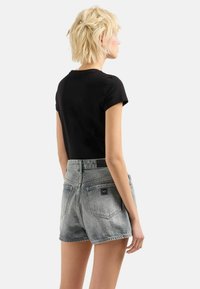 Czarny dopasowany t-shirt w połączeniu z wysokim stanem, spranymi szarymi szortami jeansowymi z dwoma tylnymi kieszeniami i oznaczeniem marki.