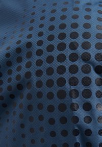 Blått tyg med ett strukturerat mönster av svarta cirkulära prickar i olika storlekar som skapar en sammanhängande design över ytan.