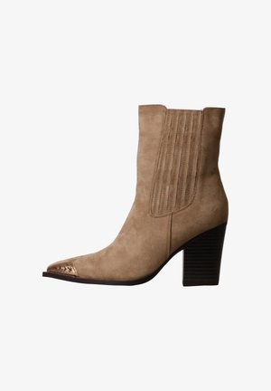 Bottine cheville en daim beige avec talon bloc empilé et empiècement élastique cousu, avec détail métallique sur l’embout pointu.