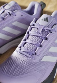 Purple athletic shoes with textured mesh upper, smooth synthetic overlays, white stripes, and matching laces on a wooden surface.