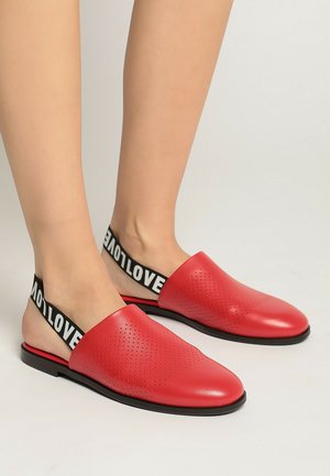 Zapatos rojos de cuero sin cordones con un diseño perforado, suela plana negra y una audaz tira elástica negra con el texto "LOVE".