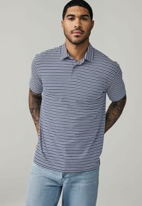 Mørkeblå og hvid stribet polo-shirt med korte ærmer og krave, parret med lyseblå jeans. Har en afslappet pasform og blød tekstur.