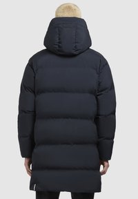 Sötétkék, puffos kabát nagy kapucnival, steppelt mintával, közepes hosszúságú fazonnal és cipzáros részlettel az alján. Sima textúra.