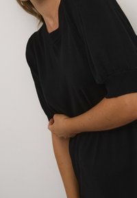 Top corto a maniche corte in maglia nera con un sottile scollo a costine e dettagli arricciati sulle spalle. Tessuto morbido, silhouette aderente e senza motivi visibili.