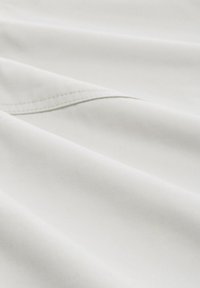 Tessuto bianco con una superficie liscia, leggermente texture e un sottile lucido, che presenta una sezione piegata con dettagli di cucitura ordinati.