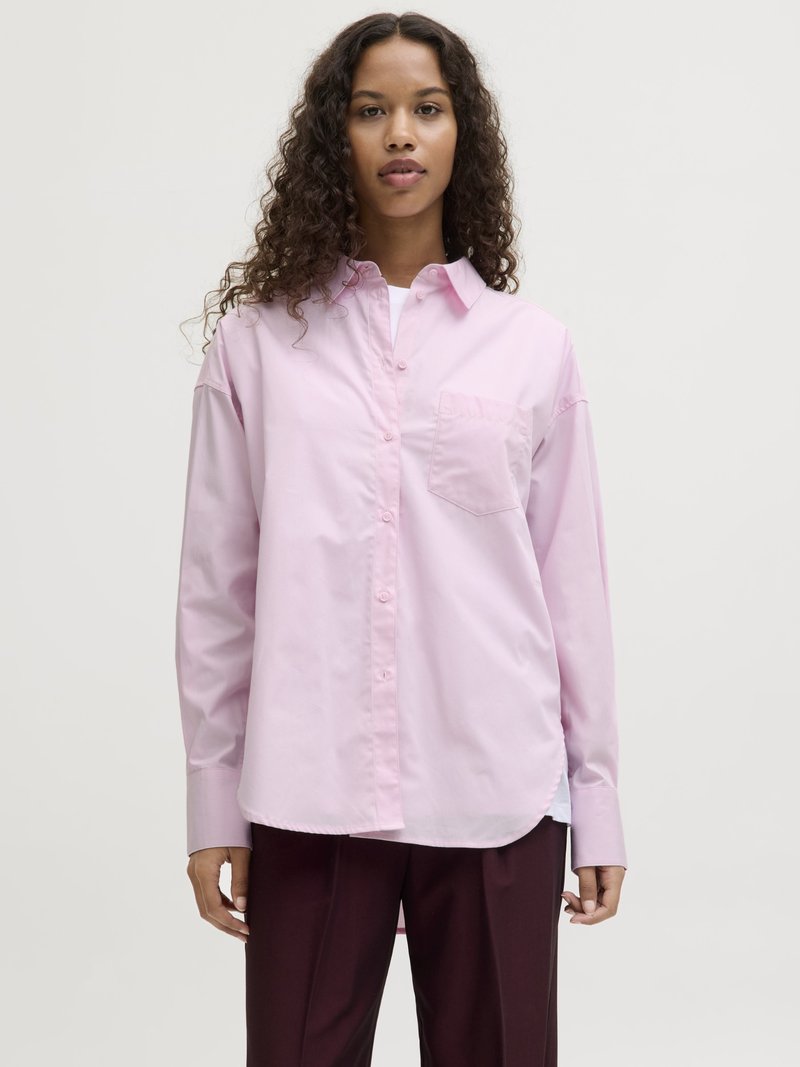 Light pink button-up shirt with a pocket, relaxed fit, and long sleeves. Made of smooth fabric with a curved hem. Paired with dark trousers.