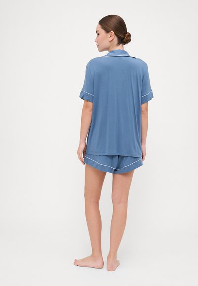 Conjunto de pijama azul com uma blusa de colarinho de mangas curtas e calções correspondentes, ambos com detalhes em branco nas costuras. Tecido suave.