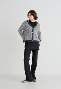 Grijze en zwarte gebreide cardigan met een V-hals, knopen aan de voorkant en geribbelde manchetten, gecombineerd met een zwarte top en wijde pijpen.