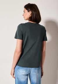 T-shirt �à manches courtes vert foncé avec encolure ronde, présentant une texture douce et une coupe décontractée, associé à un jean bleu clair.