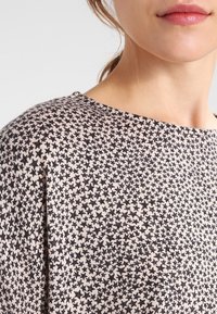 Strickoberteil mit beigem Grundton und schwarzem Sternmuster, runder Halslinie und kurzen Ärmeln. Weicher Stoff und lässiger Schnitt.