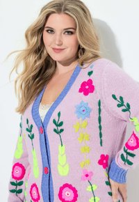 Gebreid vest met een roze lijfje, blauwe accenten en levendige bloemrijke borduurwerk in roze, blauw en groen. Twee rode knopen aan de voorkant.