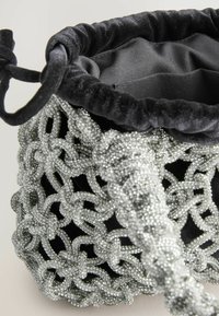 Sort fløjl drawstring taske med sølvperlearbejde, der har et indviklet vævet mønster og en blød foring indeni.