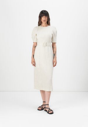 Robe midi crème avec des manches bouffantes, taille cintrée et ceinture. Tissu lisse avec une texture subtile. Associée à des sandales noires à brides.