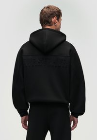 Felpa nera con cappuccio grande, caratterizzata da un testo in rilievo "WRSTBHVR" sul retro. Realizzata in un tessuto testurizzato, presenta maniche ampie e una vestibilità rilassata.