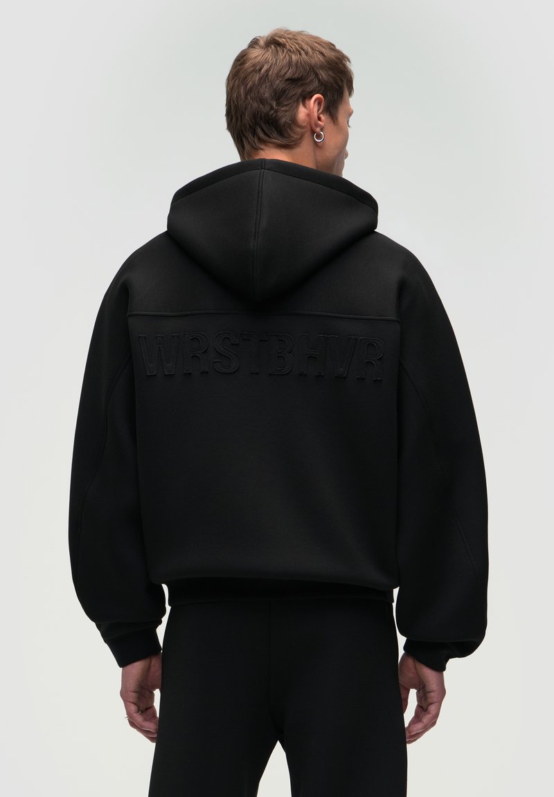 Felpa nera con cappuccio grande, caratterizzata da un testo in rilievo "WRSTBHVR" sul retro. Realizzata in un tessuto testurizzato, presenta maniche ampie e una vestibilità rilassata.