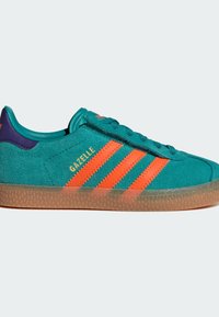 Green suede sneaker with orange stripes and lettering. Features a purple heel tab and a textured rubber sole. Classic low-top design.