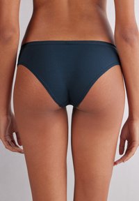 Tmavě modré bikiny s hladkou strukturou, nízkým pasem a minimálním pokrytím, se čistými liniemi a bez viditelných ozdob.