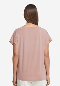 Kortärmad, rosa topp i mjukt tyg, med en avslappnad passform och rundad halsringning, med en enfärgad baksida och utan synliga mönster eller detaljer.