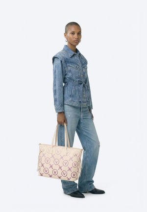 Person wearing a belted denim jacket and jeans, holding a beige tote bag with purple circular and floral patterns.