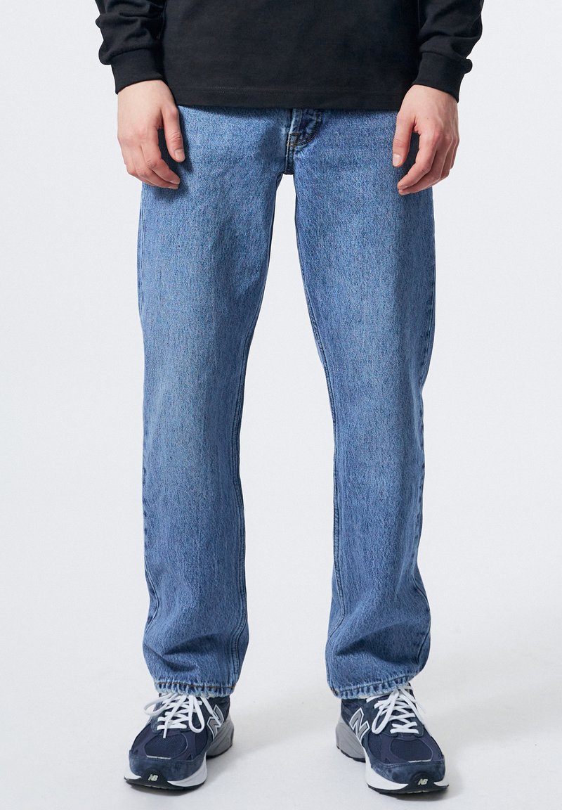 Lyseblå lige ben jeans med en falmet vask, lavet af denim, parret med mørkeblå sneakers med hvide accenter og snørebånd.