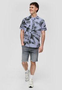 Koszula z krótkim rękawem, zapinana na guziki, w jasnopurpurowym kolorze z czarnymi wzorami liści, zestawiona z szarymi szortami typu rolled i białymi sneakersami sportowymi.