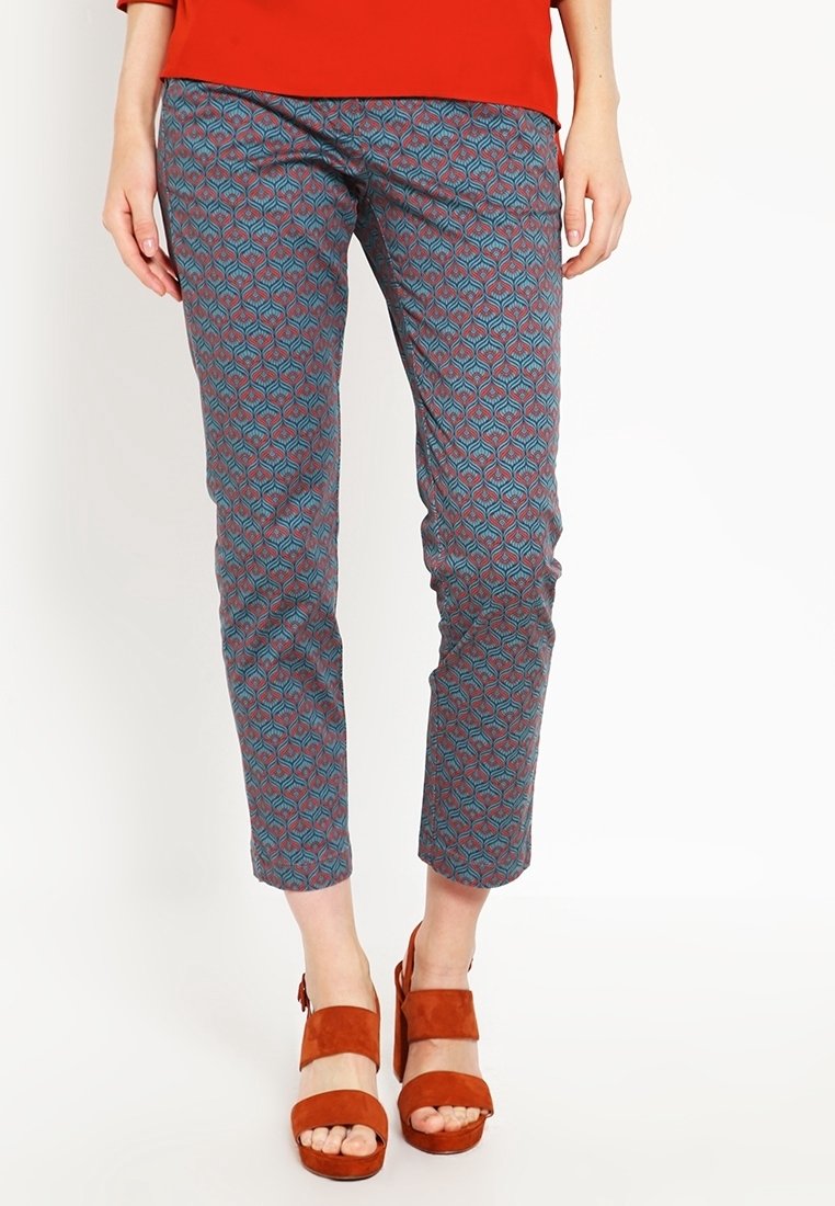 Blå mönstrade byxor med ett geometriskt mönster i nyanser av röd och teal. Slim fit med cropped längd, i kombination med bruna klackar med ankelsnodd.