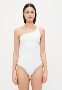 Maillot de bain blanc asymétrique avec une coupe ajust�ée, texture lisse et un branding minimaliste sur le devant. Ouvertures de jambe très hautes.