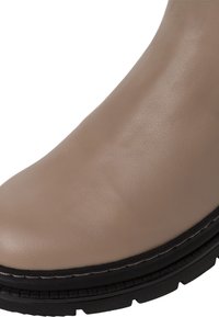 Bottine en cuir beige avec un bout arrondi, semelle en caoutchouc noire et détail de couture visible autour de la base.