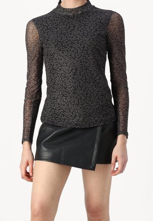 Kvinde iført en sort, langærmet mesh-top med leopardprint og en sort, asymmetrisk lædermininederdel.