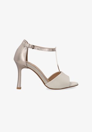 Białe i metaliczne złote sandały na wysokim obcasie z paskiem wokół kostki, designem T-bar, otwartym noskiem i gładkim wykończeniem. Posiadają smukły obcas w kształcie szpilki.