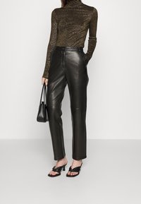 Schwarze, Leder hohe Taille Hose mit maßgeschneidertem Schnitt, kombiniert mit einem enganliegenden, bronzefarbenen Glitzer-Pullover mit Stehkragen und geknoteten schwarzen Sandalen.