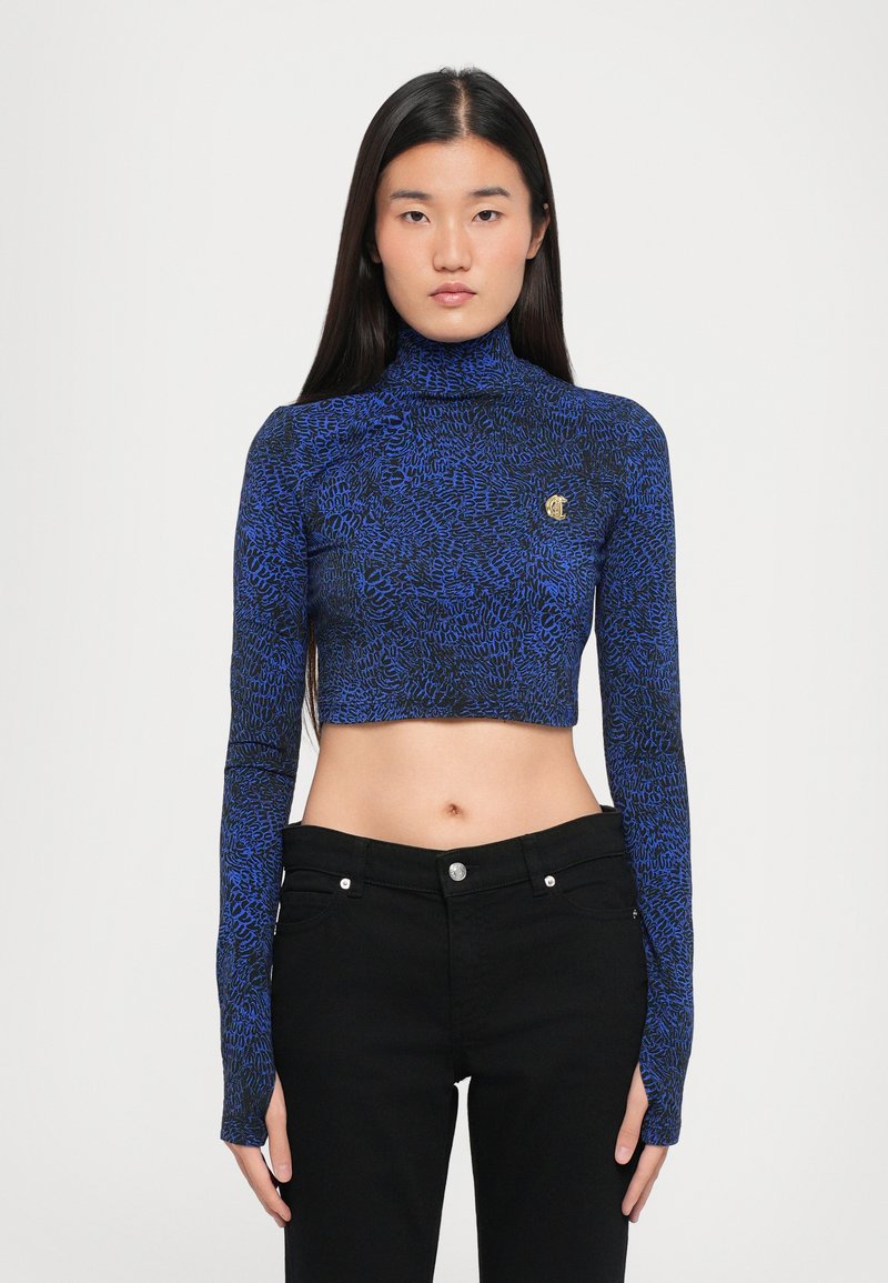 Cropped long-sleeve top in blue and black pattern, featuring a high turtleneck and a small logo accent on the chest. Paired with black pants.