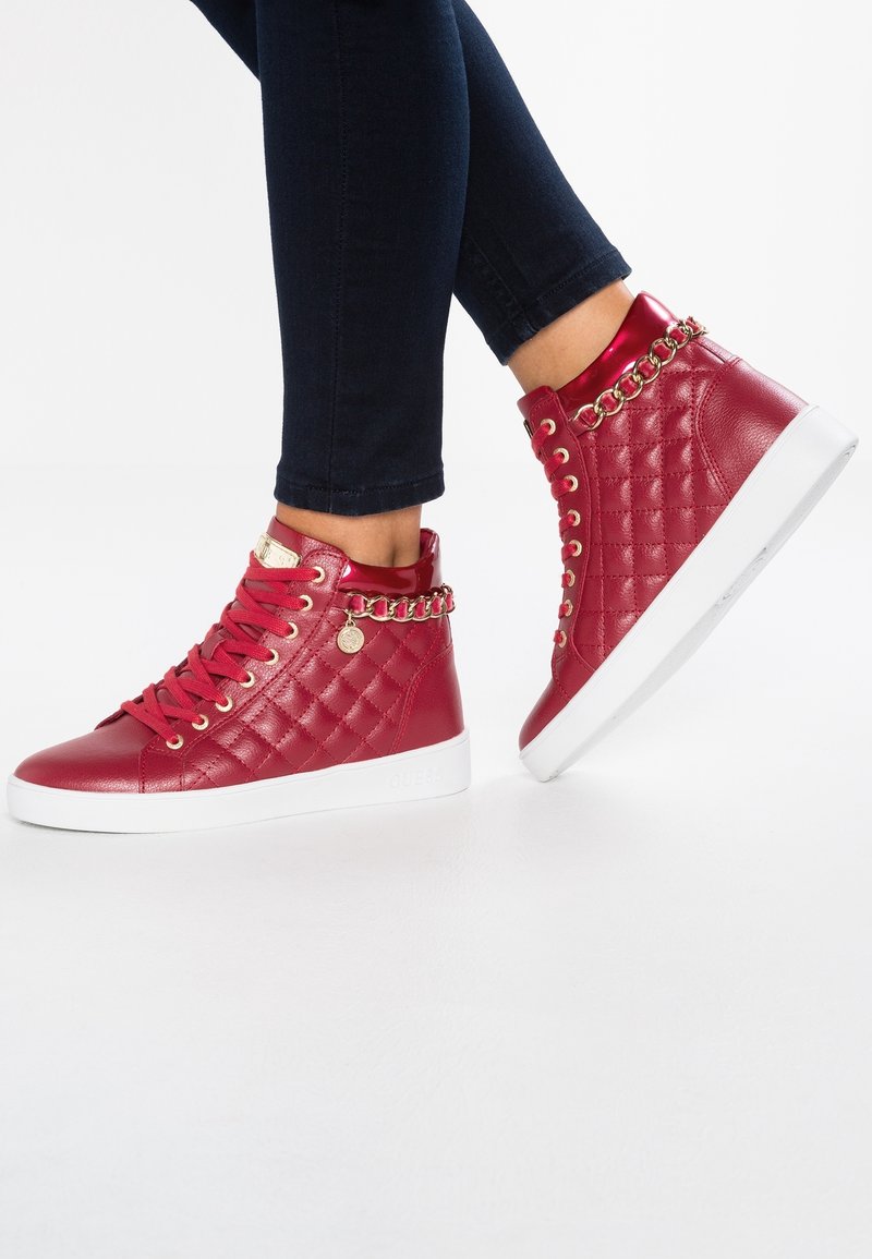 Red high-top sneakers made of quilted synthetic leather, featuring gold chain accents and a white rubber sole.