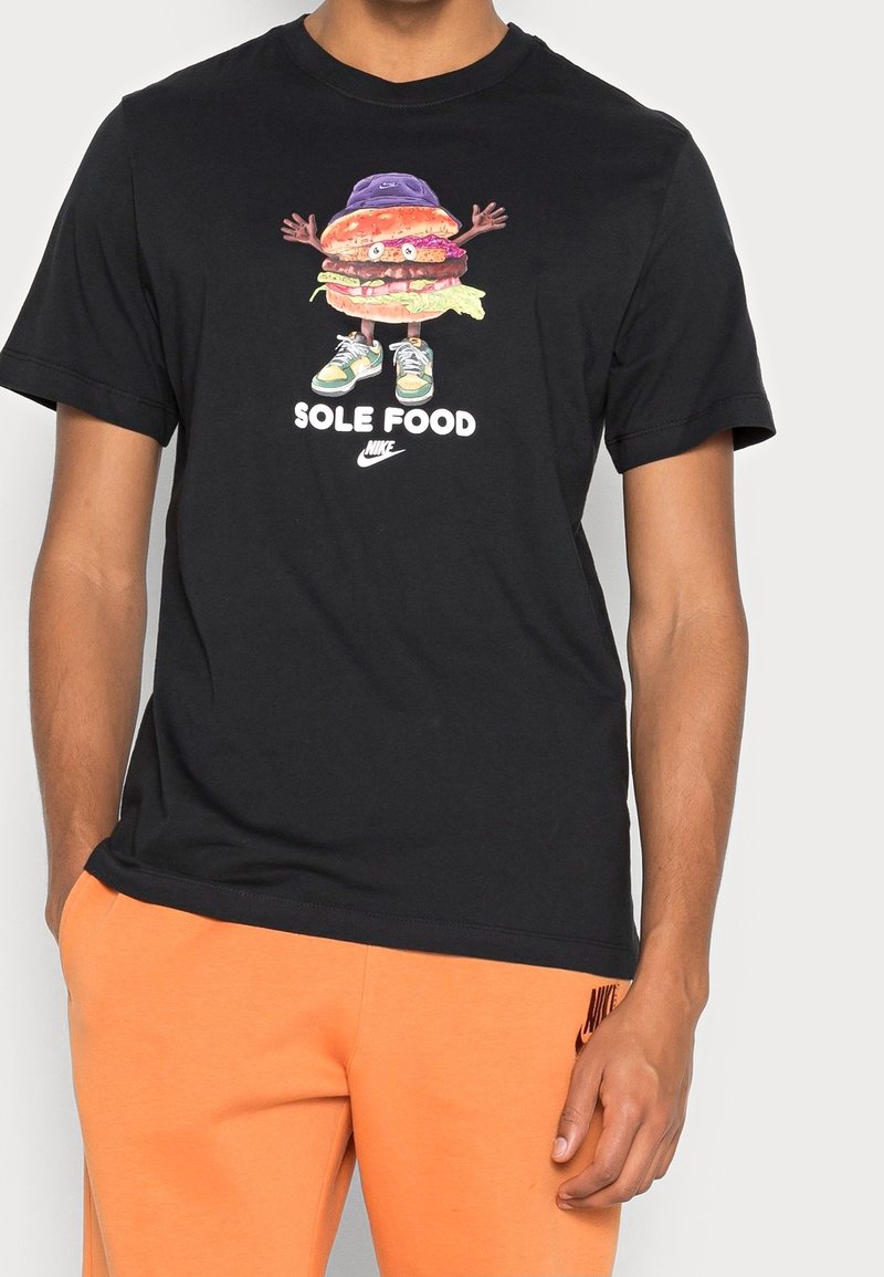 Schwarzes Baumwoll-T-Shirt mit einem bunten Burger-Grafik, der Arme hat, einen lila Hut und Turnschuhe trägt, darunter der Text "SOLE FOOD".