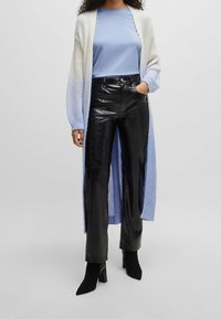 Öppen cardigan i vitt och ljusblått stickat; kombinerad med en ljusblå t-shirt med rund halsringning och högmidjade svarta läderbyxor.