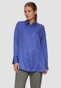 Koninklijk blauwe satijnen blouse met een puntkraag, lange mouwen, een knoopsluiting aan de voorkant en een relaxte pasvorm, gecombineerd met grijze, op maat gemaakte broek.
